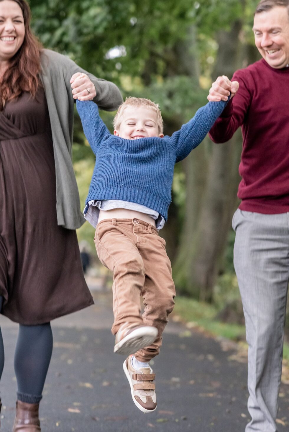 Boy swinging in parents' arms on outdoor family photo shoot in Ilkley, West Yorkshire