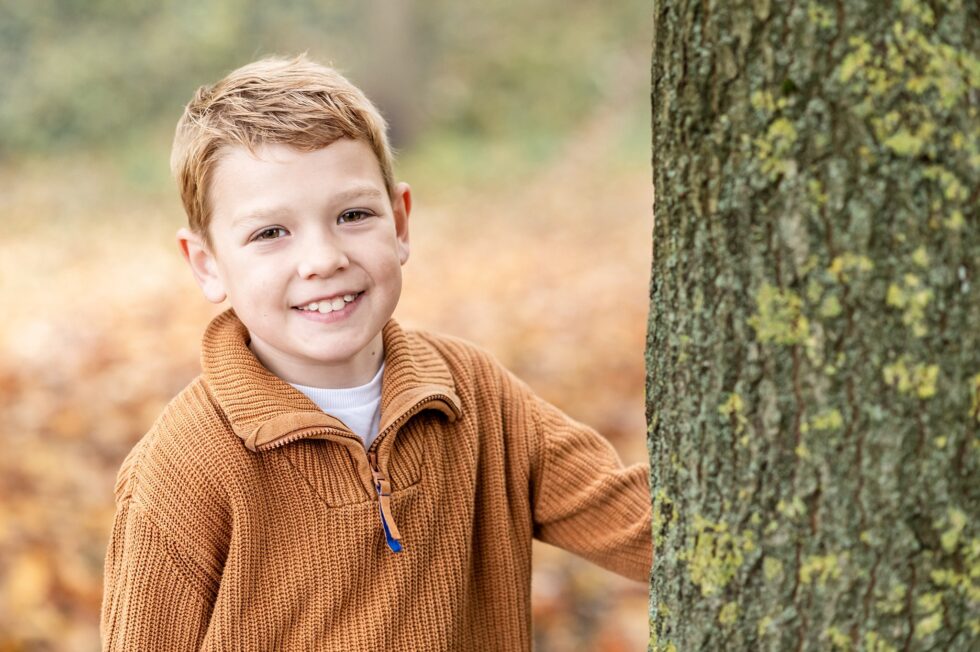 Young boy smiling from behind a tree during relaxed and natural family photo session with Skipton and Ilkley photographer