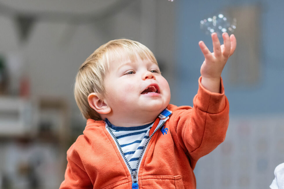 Toddler reaching for bubbles during a nursery photography session for marketing materials in Ilkley, West Yorkshire