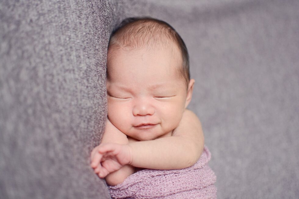 smiling newborn baby girl wrapped up in muted pink blankets during photography session in Skipton, North Yorkshire
