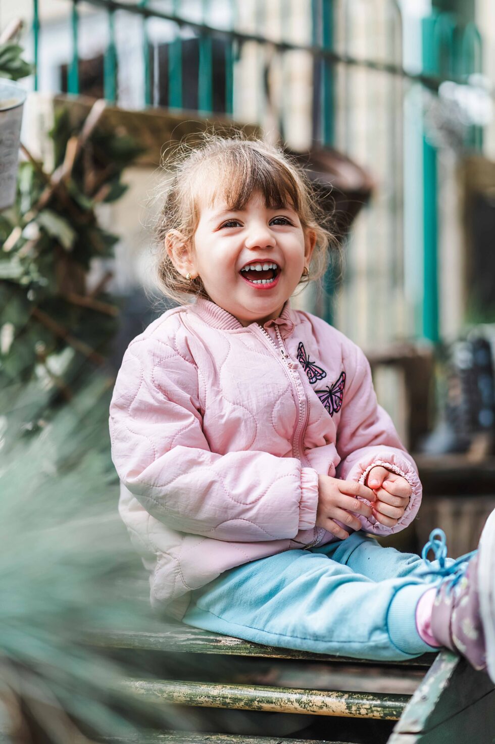 Smiling child sitting on a log at a forest school during an outdoor nursery photography session in Skipton, North Yorkshire