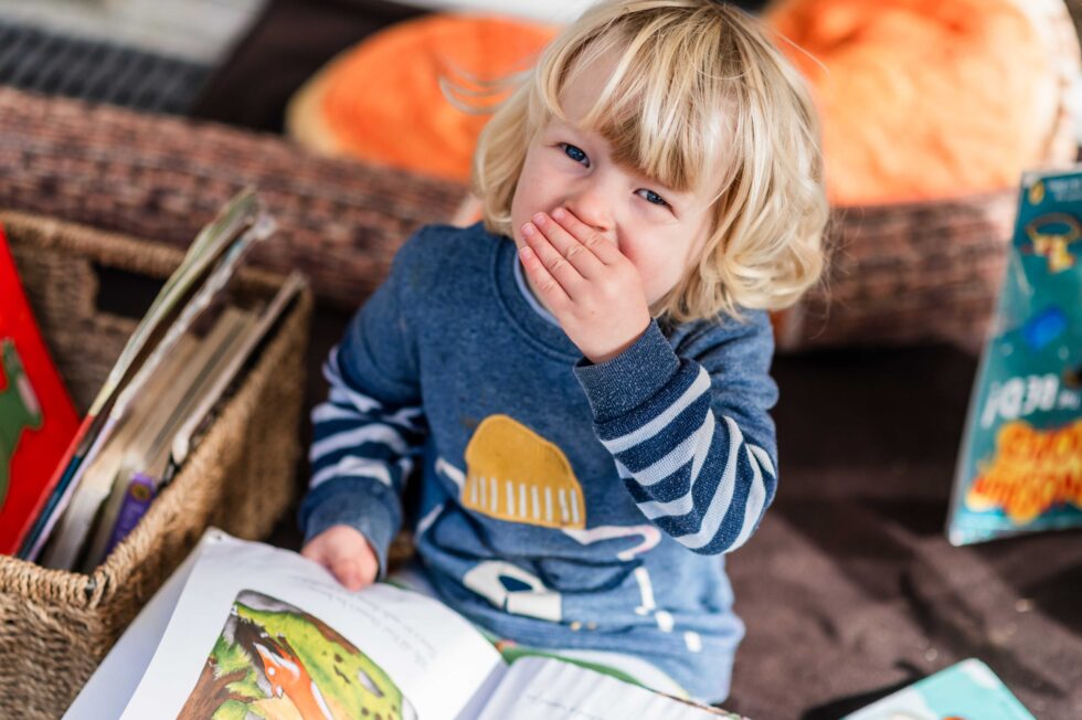 Toddler reading a book in a cozy corner during a nursery photography session for brochures in Skipton, North Yorkshire