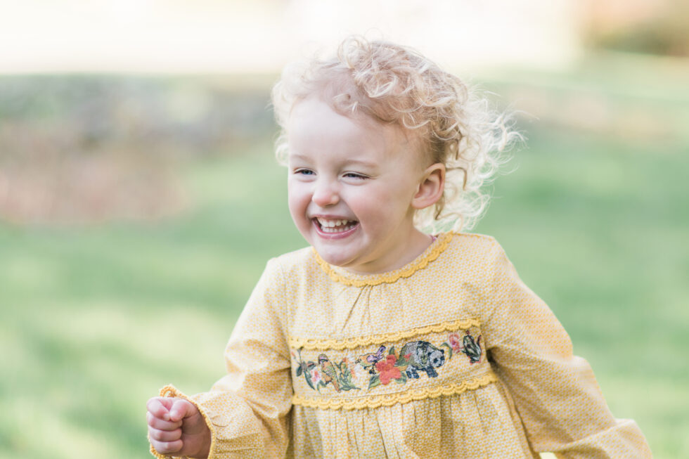 Laughing toddler in a yellow dress during a natural family photography session in Halifax, North Yorkshire