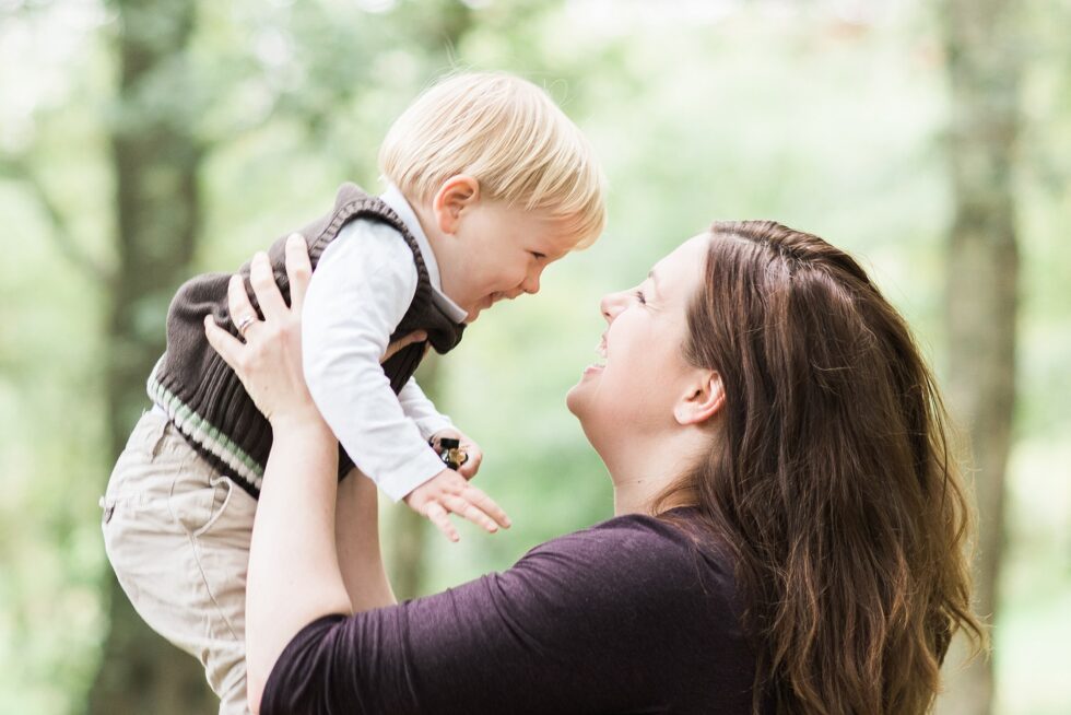 Mother lifting her toddler in the air during a joyful family photography session in the woods near Leeds, West Yorkshire