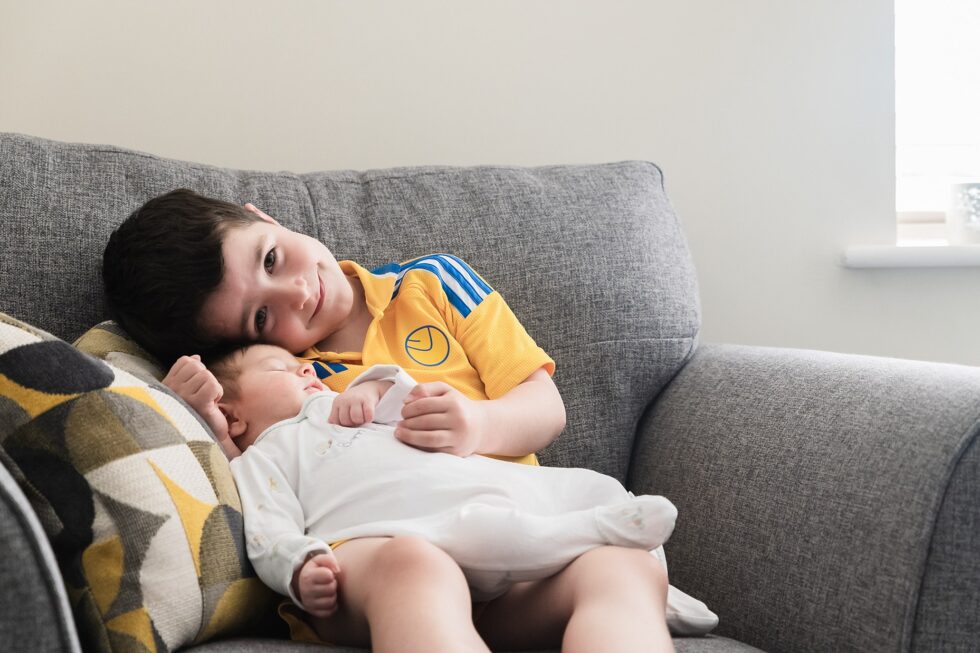 Older brother cuddling with his newborn sibling on a couch during an at-home newborn photo session in Leeds, Yorkshire